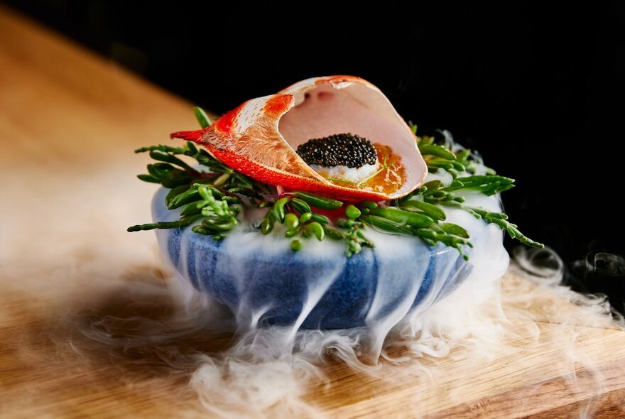 High end gourmet food presented on a blue stone dish with dry ice mist and smoke curling out from under the food.
