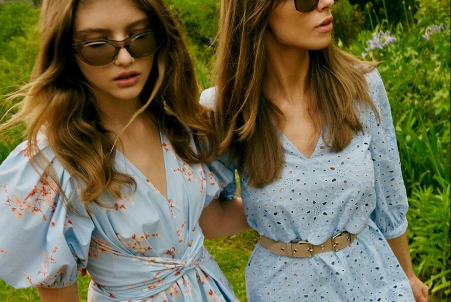 Two models in light blue dresses with garden behind.