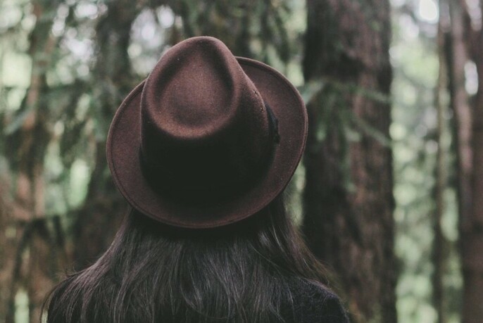 Back view of a deep red fedora-style hat on a person with long dark hair, trees in background.