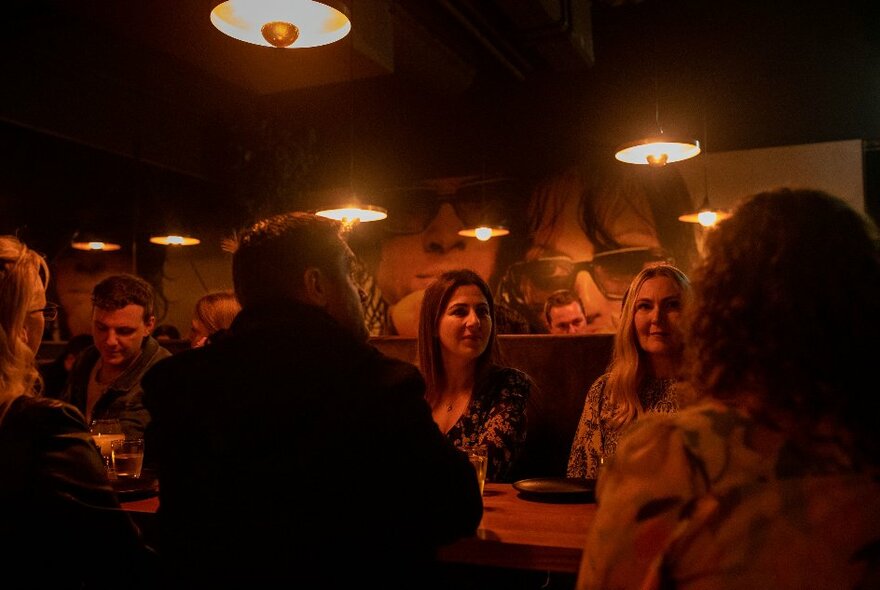 People seated at a bar in a dimly lit bar with low hanging lighting.