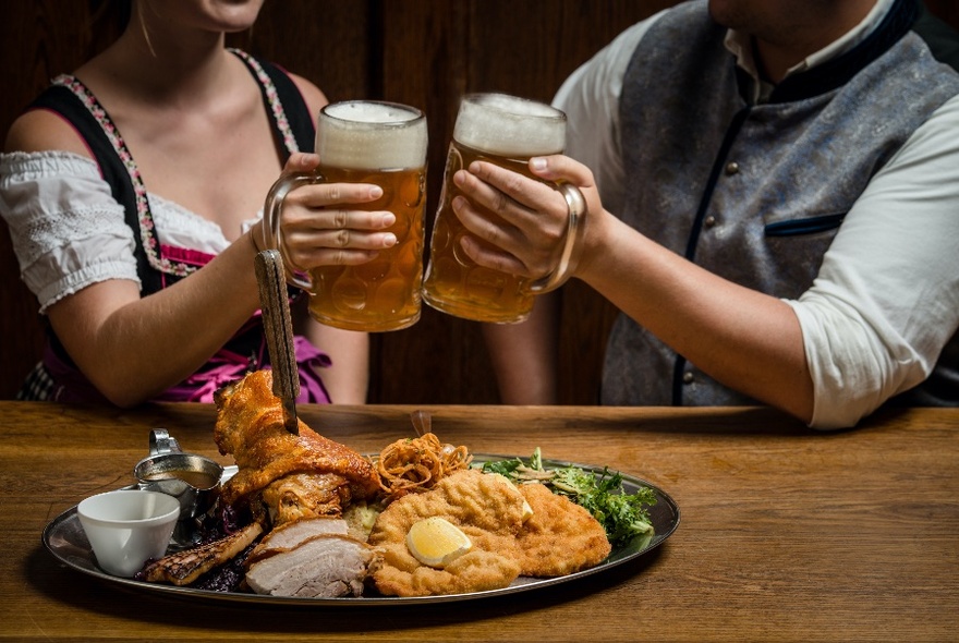Couple wearing traditional German costume, enjoying beer and  about to eat a giant schnitzel and chips.