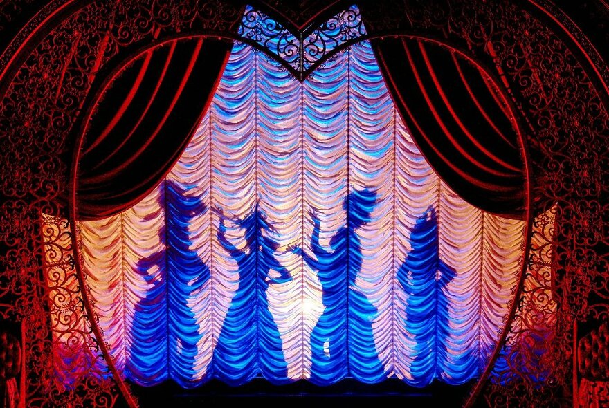 Four shadowy figures behind a theatre curtain.