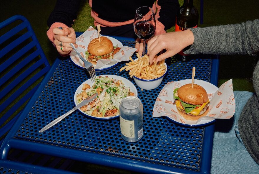 People seated at a blue outdoor table eating fries and burgers.