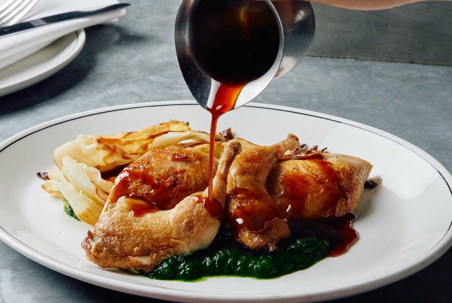 Plate of roast chicken, on a bed of pureed greens with a side of fries, with gravy being poured from a jug onto the plate.