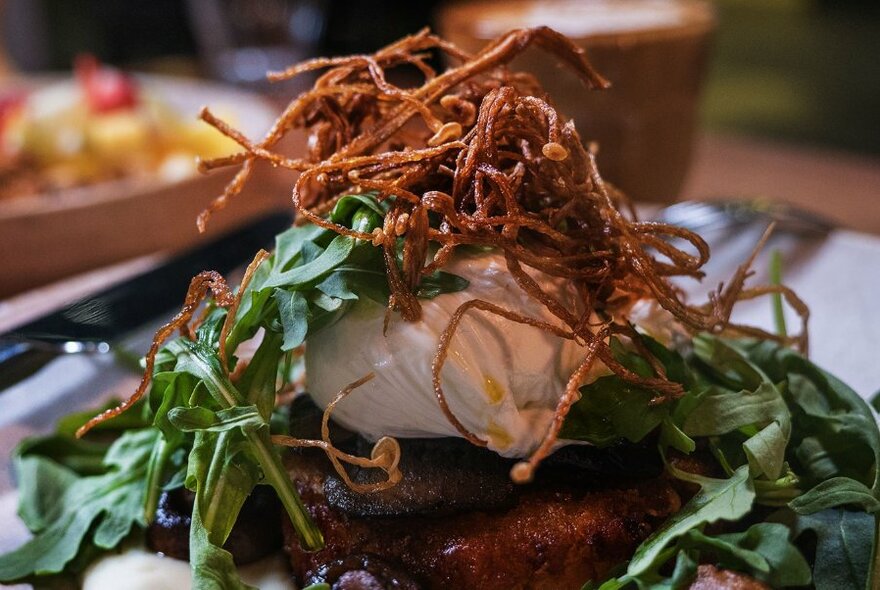 A plate of food tooped with a poached egg, rocket and deep fried onions.