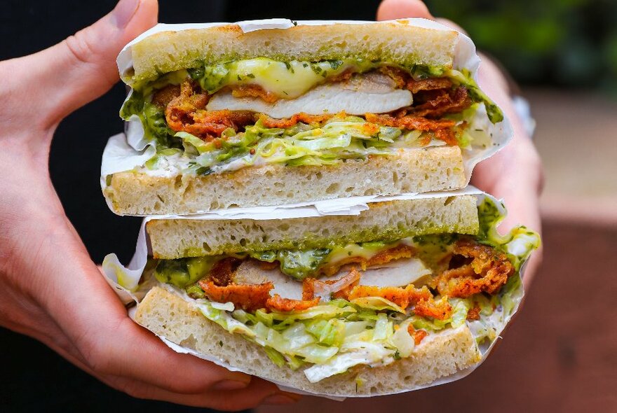 Generously filled sandwich halves, wrapped in paper, held with fillings showing.