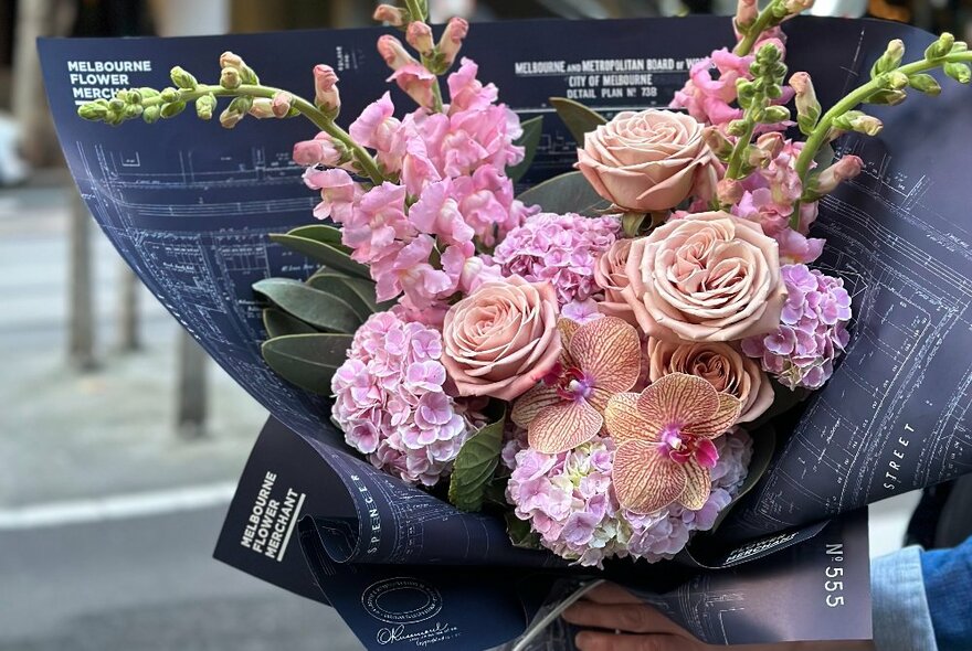 Floral bouquet in shades of pink and green wrapped in distinctive branded dark paper.