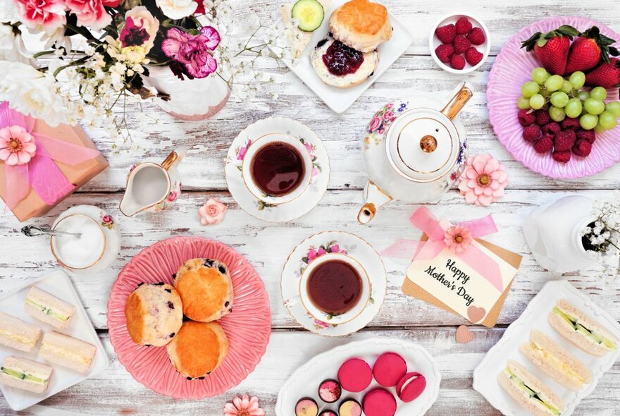 Bird's eye view of a table filled with savoury and sweet treats on plates, cups of tea in fine china and a vase of flowers.