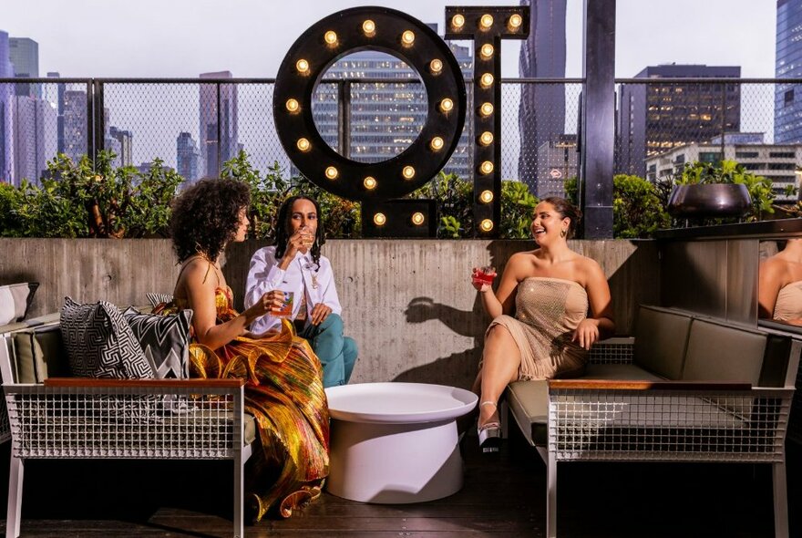 People seated outside at a rooftop bar with illuminated QT signage and city buildings in the background.