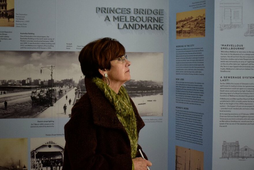 A person reading the descriptive wall panels of an exhibition displayed on the walls of a museum. 
