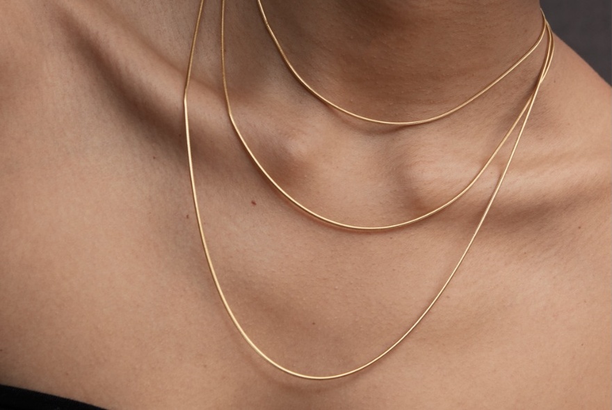 Close-up a woman's bare neck and chest area displaying three fine gold necklaces. 