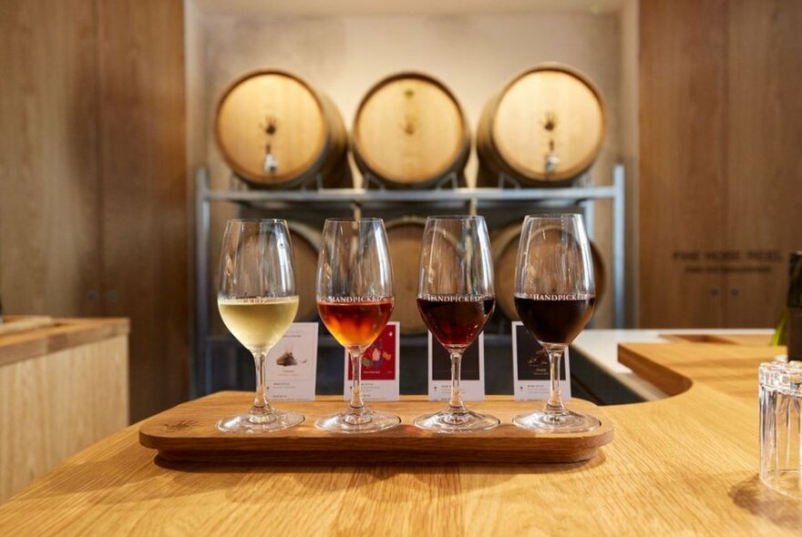 Four wine glasses on a table with wooden barrels behind them
