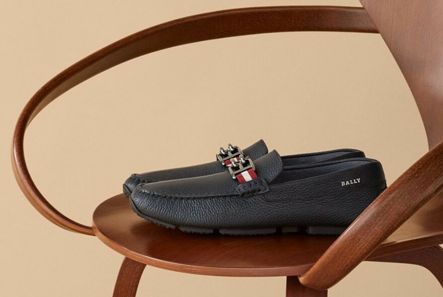 A pair of dark blue loafers on a wooden chair. 