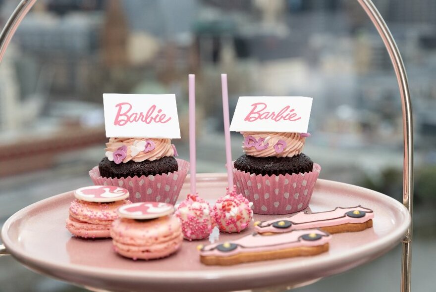 High tea plate with two pink and white cupcakes with Barbie labels, two pink macarons, two pink car-shaped cookies and two round pink treats.