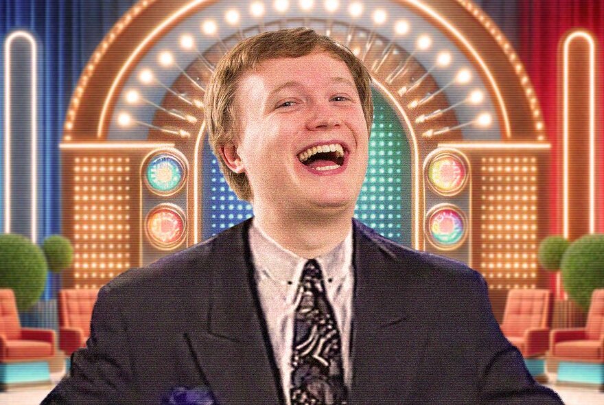 Man wearing a 1990s suit and tie, smiling, posed in front of a TV game show style set.