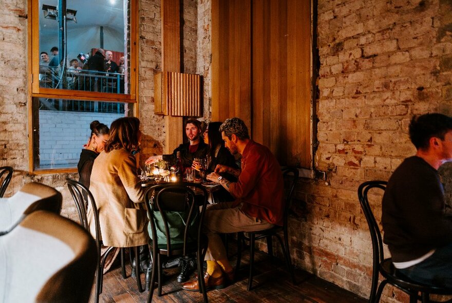 People gathered at a corner table sharing drinks in a brick walled old building. 