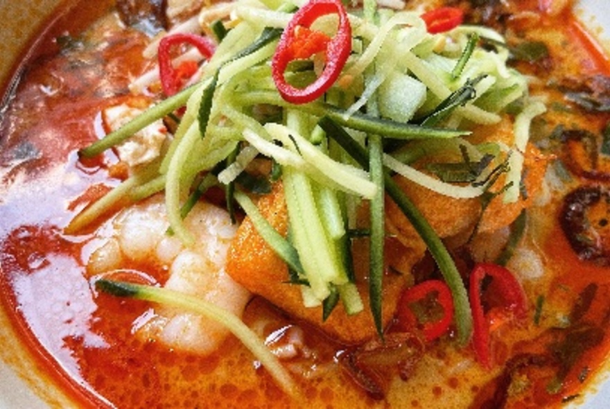 Malaysian chilli soup dish topped with garnishes.