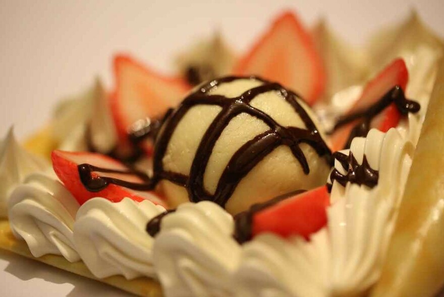 A crepe with piped cream, strawberries, ice cream and chocolate sauce.