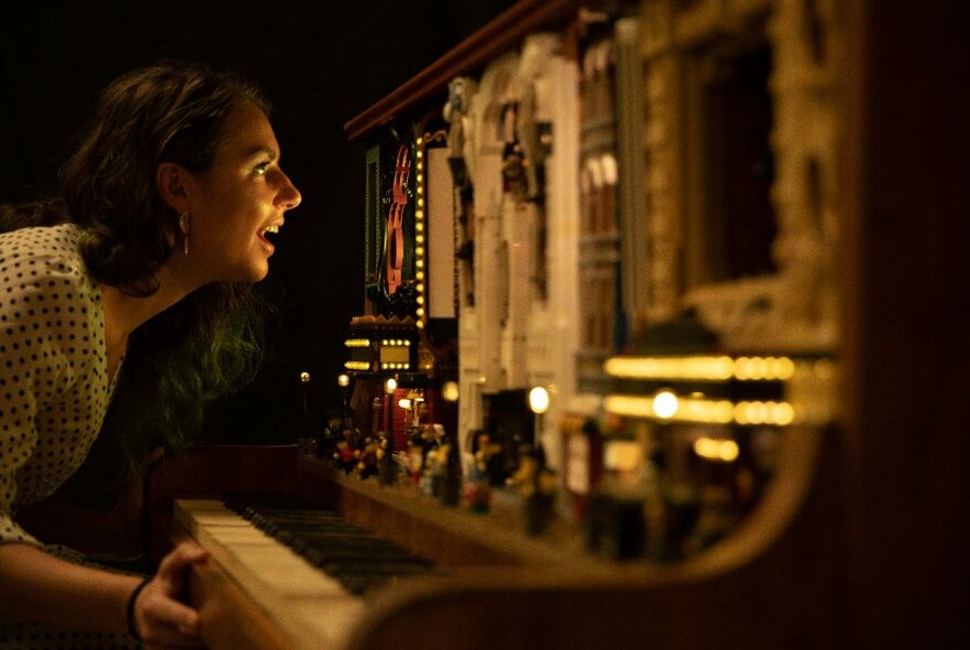 Person seen from right side, crouching over and looking in wonder at a tableau inside an upright piano.