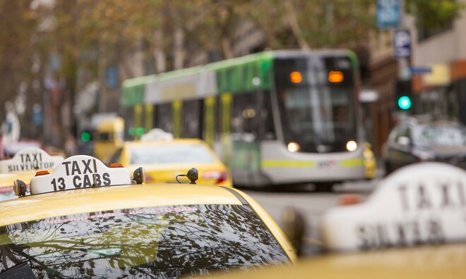 Row of yellow taxis on a street and a tram in the background. 