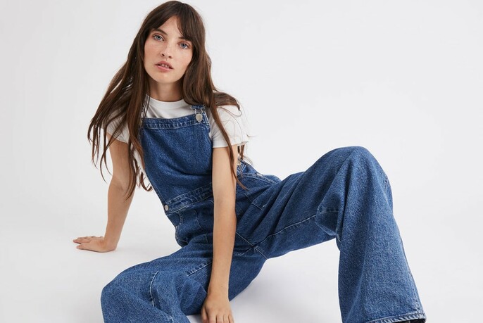 Model with long dark hair wearing flared denim overalls.