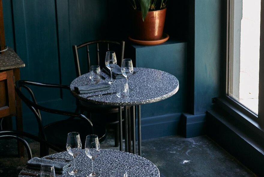 Terrazzo tables in a darkly painted restaurant set with glasses and cutlery.