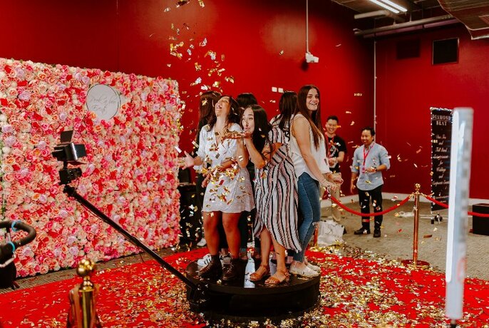 Women standing on a podium while confetti is falling on them in a red room.