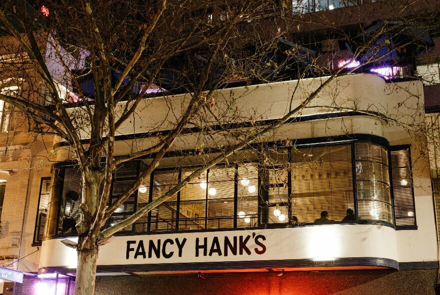 Exterior of Fancy Hanks restaurant at night, showing signage painted on the wall under the windows.