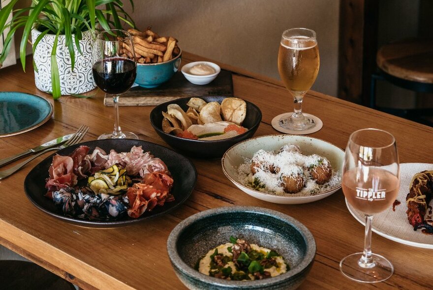 A laden table set with varied tapas style dishes and beer and wine glasses and a plant.