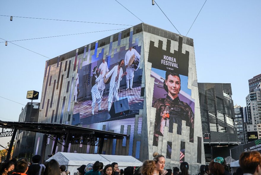 Images displayed on the big screen at Fed Square, with a crowd of people moving around underneath; part of the Korea Festival.