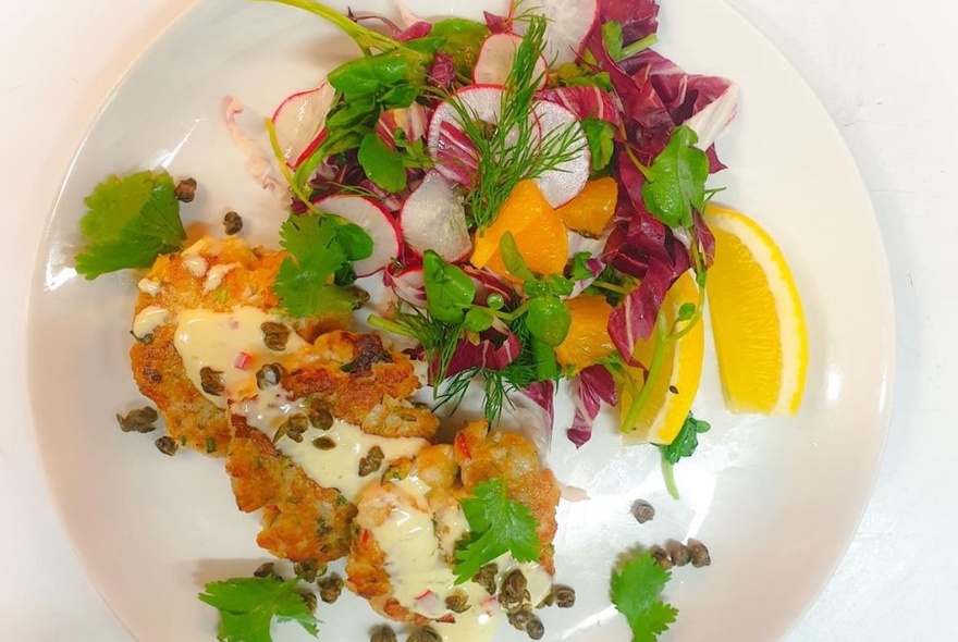 White plate with Thai fish cakes and orange and radicchio salad, with lemon wedges.