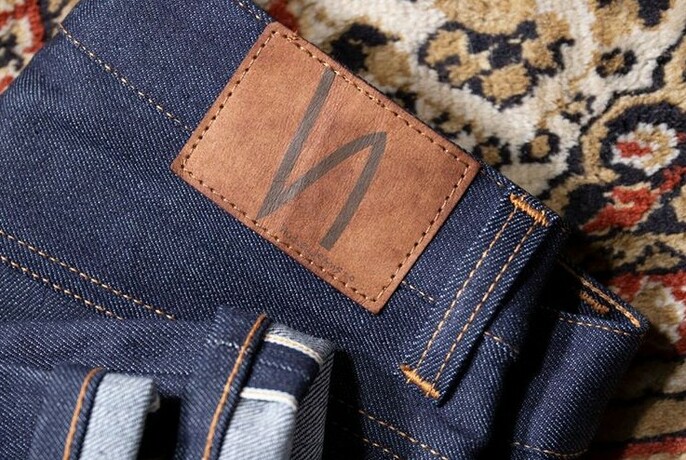 A pair of Nudie jeans on a carpet, focused on the Nudie label.