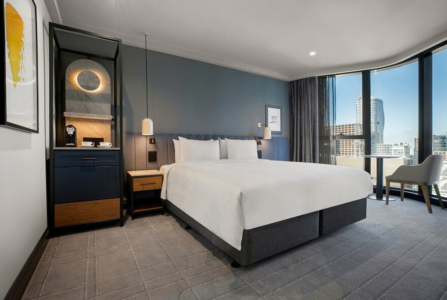 Hotel room at Voco Melbourne Central, with large floor to ceiling windows, a king size bed and elegant furnishings.