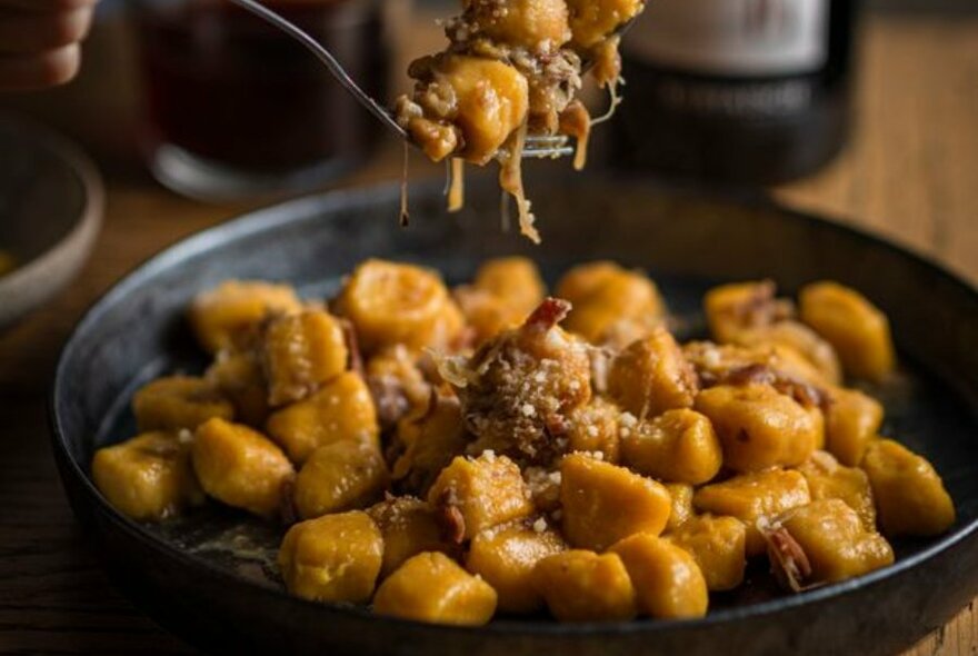Pumpkin gnocchi in a black bowl on a wooden table. Some of the  gnocchi is being lifted up with a fork.