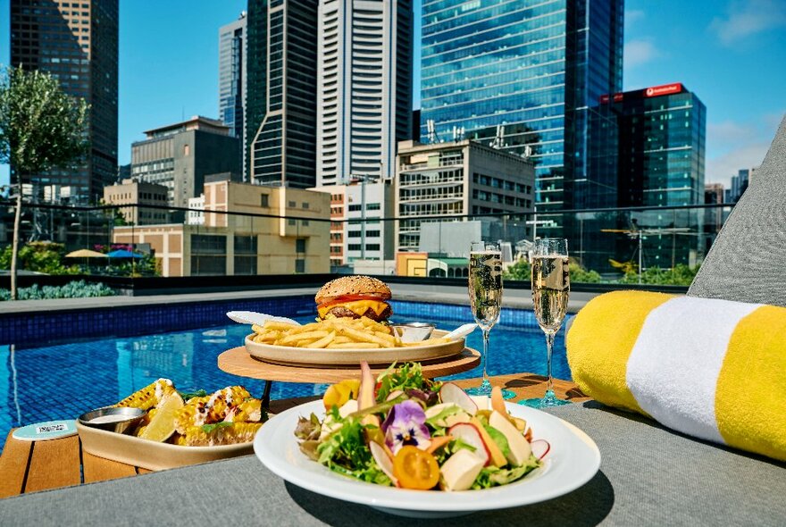 Plates of food and champagne on a poolside sun lounge. 