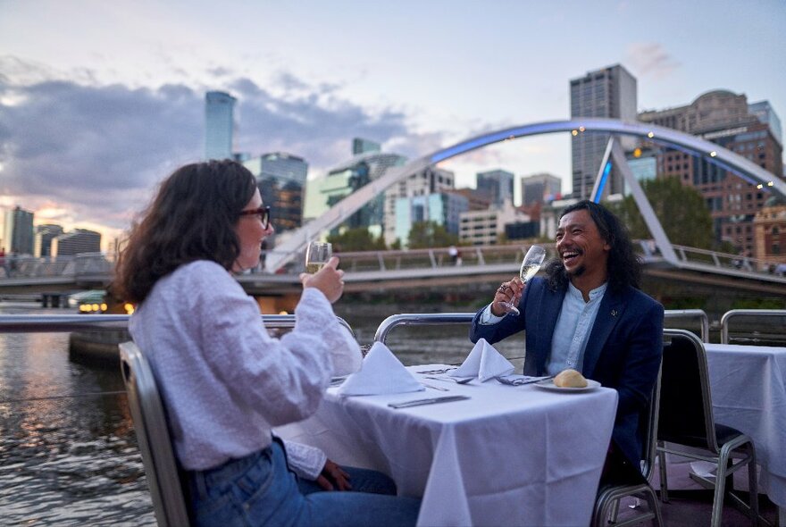 A couple enjoying a glass of wine at a table on the outdoor deck on a floating river cruise.