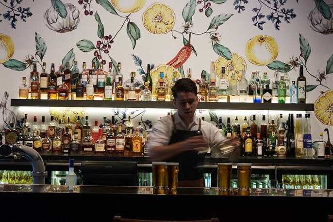 Backlit bar against floral wallpaper with bar tender pouring drinks.