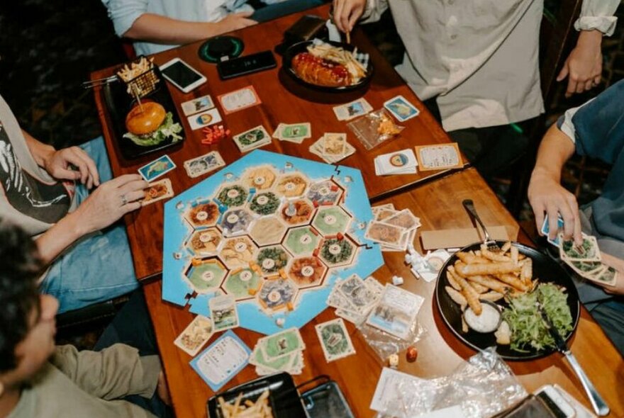 A group of friends playing Settlers of Catan with plates of pub food.