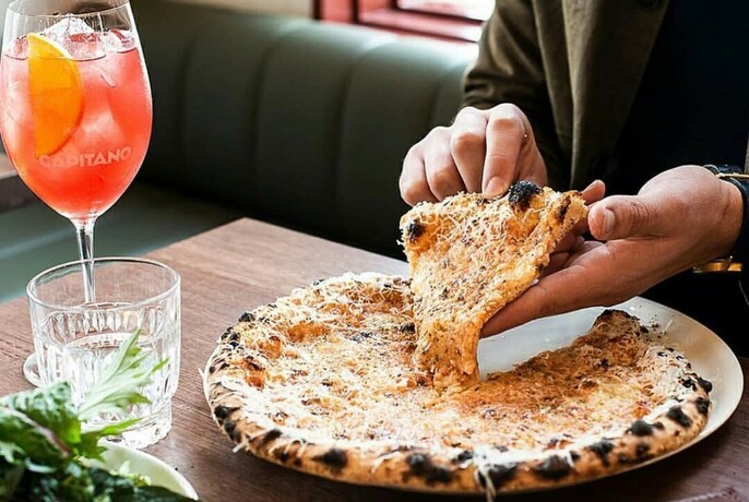 Person eating pizza and a glass of Aperol Spritz.