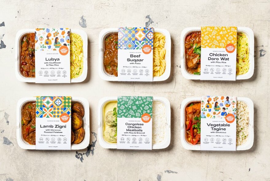 Six pre-packaged take-home meal packs on display on a table, overhead view.