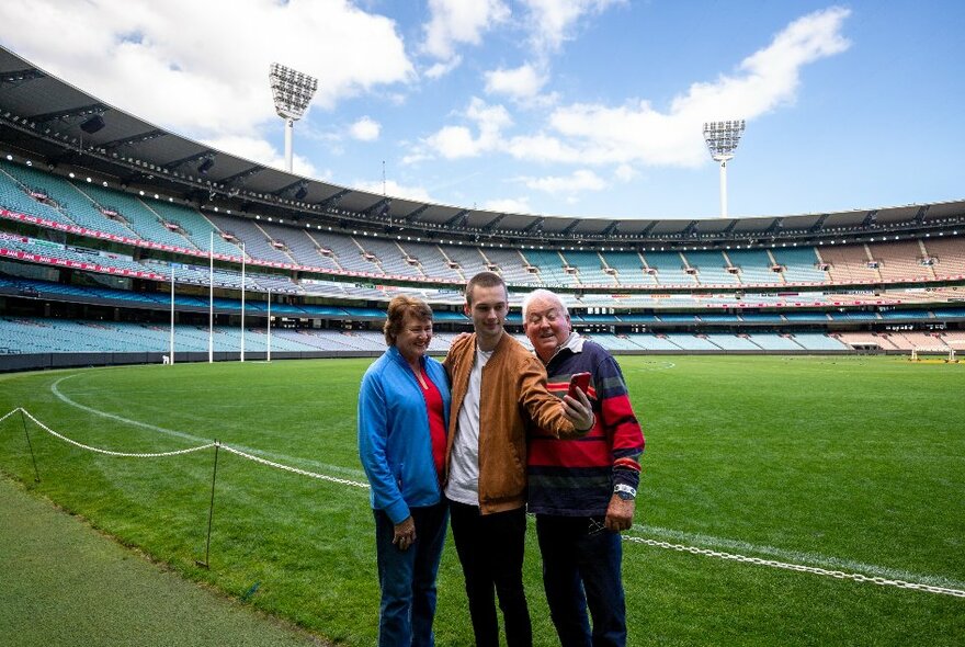 Three people standing for a selfie on the ground at the MCG.