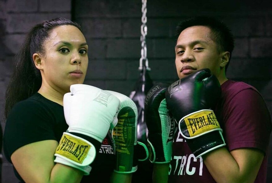 Two people wearing boxing gloves and facing the camera.