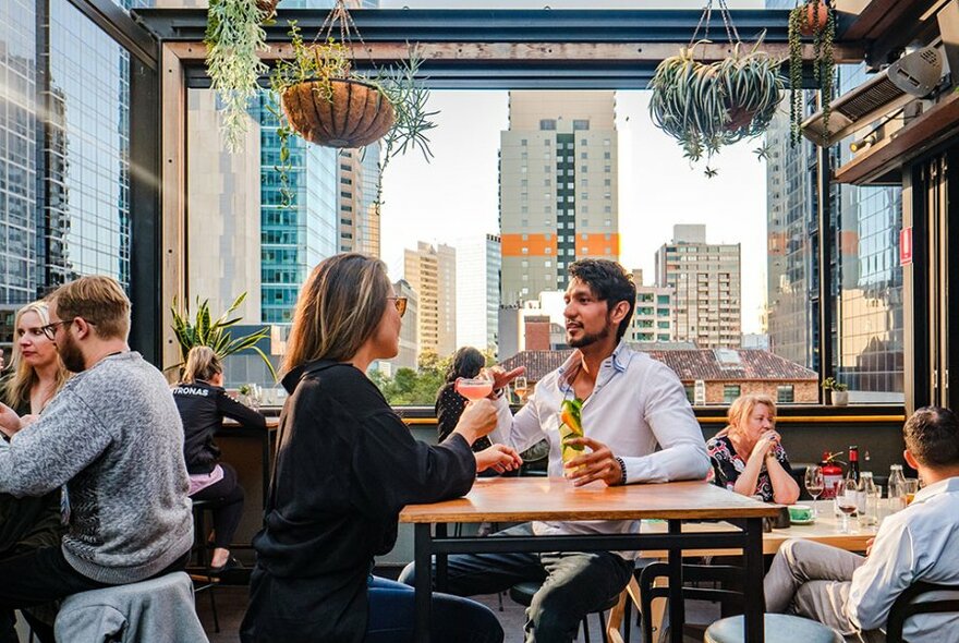 A couple dining on a rooftop bar with plants hanging from the rafters.