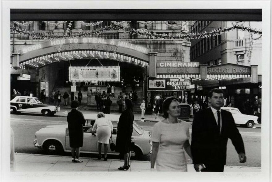 A black and white photo of people milling about outside a theatre