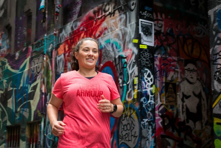 Woman in red singlet running through a laneway that is covered in street art.