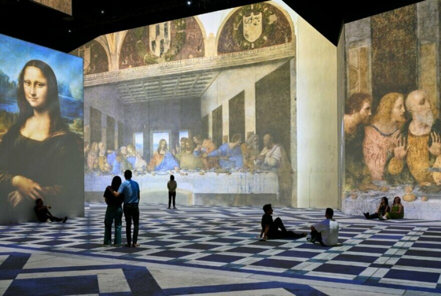People in an immersive gallery of oversized Leonardo do Vinci artworks including the Mona Lisa and Last Supper.