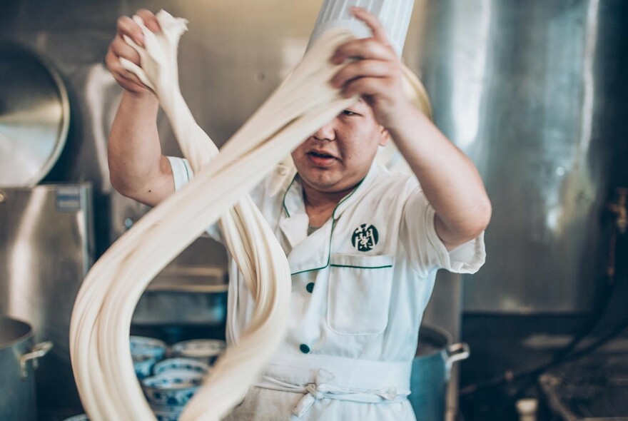 A chef twisting long pieces of noodle dough in a kitchen.