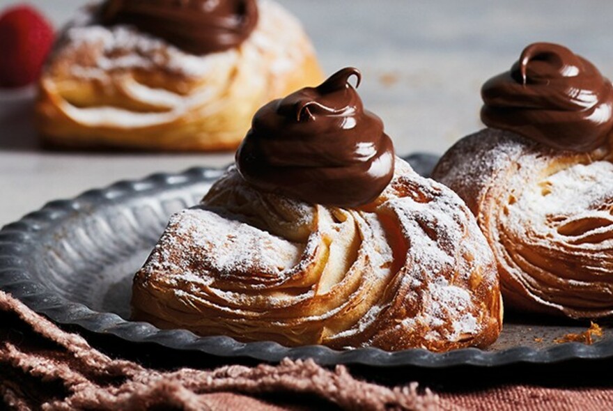 Plate with pastries dusted with icing sugar and topped with piped chocolate.