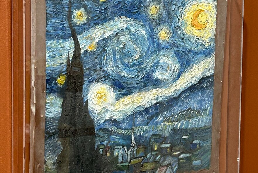 A reproduction of Vincent van Gogh's Starry NIght famous painting, recreated in chocolate, displayed on a wall behind glass.