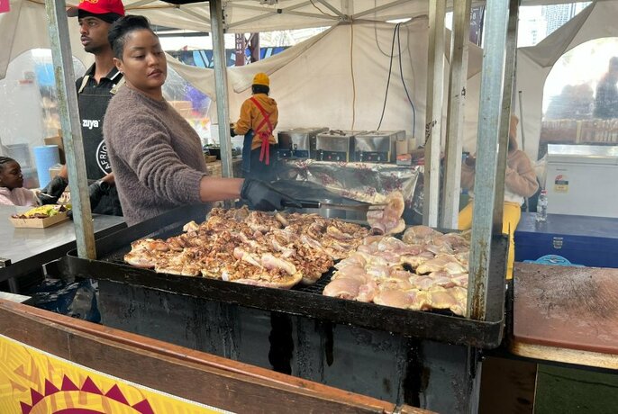 A person grilling food at an outdoor market food stall.
